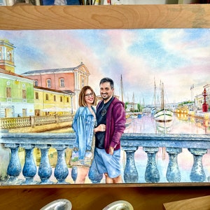 May include: Watercolour painting of a couple standing on a bridge in a European city. The couple are dressed in casual clothing and are smiling. The city is in the background, with buildings and boats visible. The painting is done in a realistic style and has a warm, inviting feel.