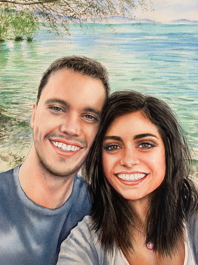May include: A watercolour painting of a couple smiling at the camera. The man is wearing a blue shirt and the woman is wearing a white shirt with a silver necklace. They are standing in front of a body of water with trees in the background.