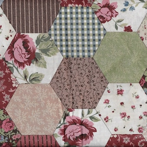 Puede incluir: Una tela con un diseño de patchwork que presenta formas hexagonales en varios patrones florales, incluyendo rosas rosas, paisley y cuadros. La tela es en tonos de marrón, verde, rosa y blanco.