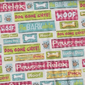 Może przedstawiać: Biała tkanina z kolorowymi prostokątnymi blokami z psimi frazami, takimi jak "Paws and Relax" i "Woof". Bloki są w kolorach różowym, zielonym, niebieskim i żółtym, z odciskami łap i ilustracjami kości.