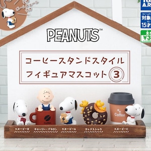 Puede incluir: Un conjunto de cinco figuras de personajes de Peanuts, incluyendo a Snoopy, Charlie Brown y Woodstock. Las figuras se exhiben en un estante de madera frente a un letrero con forma de casa con el texto PEANUTS y caracteres japoneses. Cada figura presenta un accesorio temático de café.