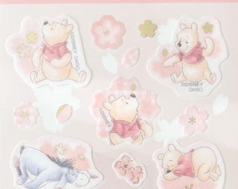 May include: A sheet of Disney Design Stickers featuring Winnie the Pooh and Eeyore characters in various poses, surrounded by pink cherry blossom motifs and small gold-colored flower accents. The packaging includes the text Disney Design Stickers.