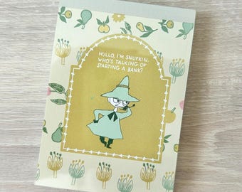 May include: A rectangular notepad featuring a light green and yellow color palette with a central illustration of a character wearing a wide-brimmed hat. The text reads, HULLO, I'M SNUFKIN. WHO'S TALKING OF STARTING A BANK? The border has floral motifs.
