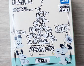 May include: A square cardboard box featuring Peanuts 75th anniversary branding with a white background and light blue accents. The front displays a black and white illustration of Snoopy characters stacked in a pyramid, with Japanese text and the Takara Tomy Arts logo.