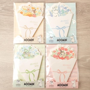 Könnte beinhalten: Vier Packungen Briefpapier im Moomin-Design. Jede Packung zeigt ein Bouquet-Design mit verschiedenen Blumenarrangements und Moomin-Charakteren. Das Briefpapier ist in durchsichtigem Kunststoff verpackt, mit dem Moomin-Logo und Text.