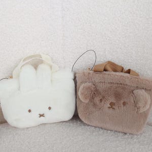 May include: Two plush, cartoon-style bags. One is white and shaped like a bunny with floppy ears and a small hat. The other is brown and shaped like a bear. Both have small handles and embroidered facial features.