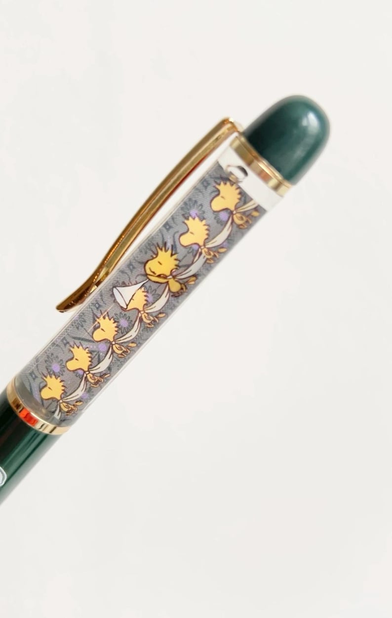 May include: A green and gold pen with a decorative barrel featuring a repeating pattern of yellow cartoon birds. The pen has a gold clip and a dark green top.