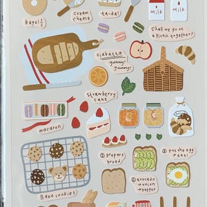 May include: A sheet of Suatelier stickers with a bread theme. The stickers include images of bagels, ciabatta, cookies, bread, and breakfast items like eggs, avocado toast, and a toaster. The text "i like bread" is also present.