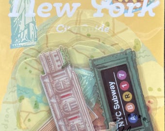 May include: A clear sticker sheet with a New York City theme. The sheet includes illustrations of the Statue of Liberty, a burger with a flag, a subway sign, and city buildings. The text "New York City Guide" is also visible.