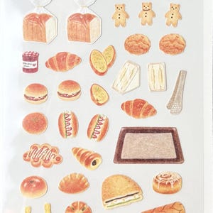May include: A sheet of "DAILY DECO STICKERS" featuring illustrations of bakery items. The stickers include bread, croissants, sandwiches, pastries, and cakes. The color palette is warm, with shades of brown, yellow, and white. The sticker sheet is labeled "1177: old bakery."