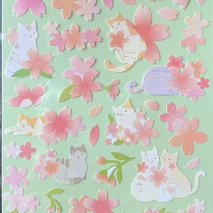May include: Sheet of stickers featuring cat illustrations and cherry blossoms in shades of pink, orange, and white. The text "NEKONI" and Japanese characters are at the top. The stickers are on a light green background.