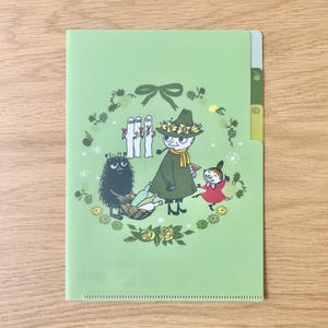 May include: A light green plastic document folder featuring a printed illustration of Snufkin, Little My, a hairy creature, and three white ghosts surrounded by a floral wreath. The folder has multiple internal tabs visible on the right side.