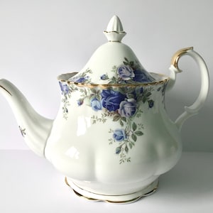 May include: A white porcelain teapot with a lid, adorned with blue rose floral patterns and gold trim. The teapot features a curved spout and a handle with gold accents. A classic piece for serving tea.
