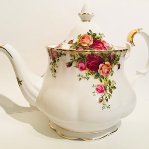 Può includere: Teiera in porcellana bianca con un motivo floreale di rose nei toni del rosa, rosso e pesca. La teiera ha finiture dorate sul bordo, sul manico e sul beccuccio. Il coperchio è sormontato da un pomello dorato.