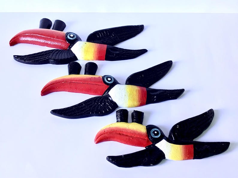 May include: Four decorative toucan birds. Each toucan features a red beak, black wings, and a yellow, red, and white chest. The toucans are displayed against a white backdrop.