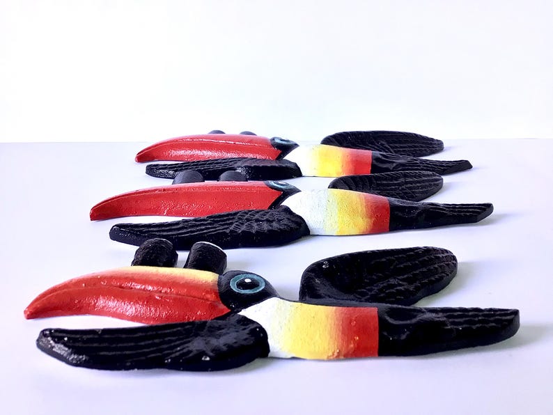 May include: A collection of wooden toucan ornaments. Each toucan features a vibrant red beak, a black body, and accents of white, yellow, and red. The toucans are displayed in a row, highlighting their colourful details. Ideal for home decoration.
