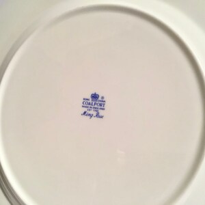 May include: The bottom of a white ceramic plate with a blue and white logo that reads "Bone China Coalport Made in England Est 1750 Ming Rose"