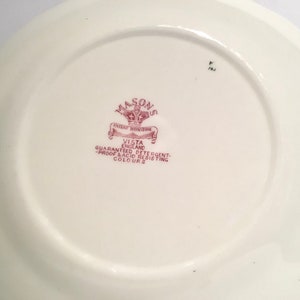 May include: Close-up of the back of a white ceramic plate with a red and white logo that reads "Mason's Patent Ironstone Vista England Guaranteed Detergent-Proof & Acid Resisting Colours".