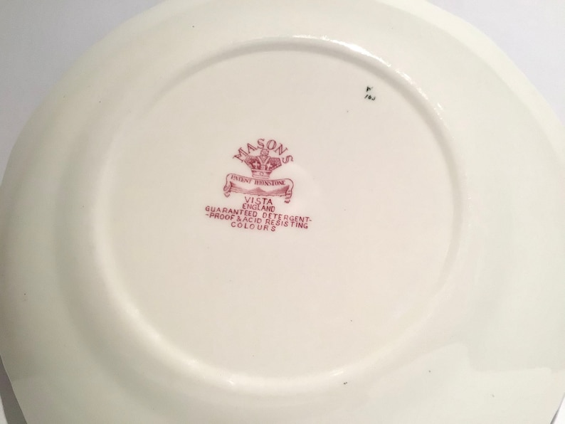 May include: Close-up of the back of a white ceramic plate with a red and white logo that reads "Mason's Patent Ironstone Vista England Guaranteed Detergent-Proof & Acid Resisting Colours".