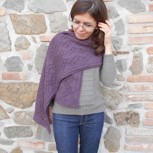 Può includere: Una donna indossa uno scialle di maglia viola e grigio con un motivo a pizzo. Indossa jeans blu e ha i capelli castani.