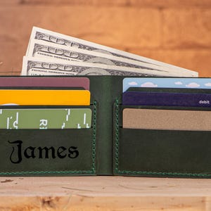 May include: A dark green leather wallet with a stitched border. The wallet has multiple card slots and a cash pocket. The name "James" is embossed on the front of the wallet.