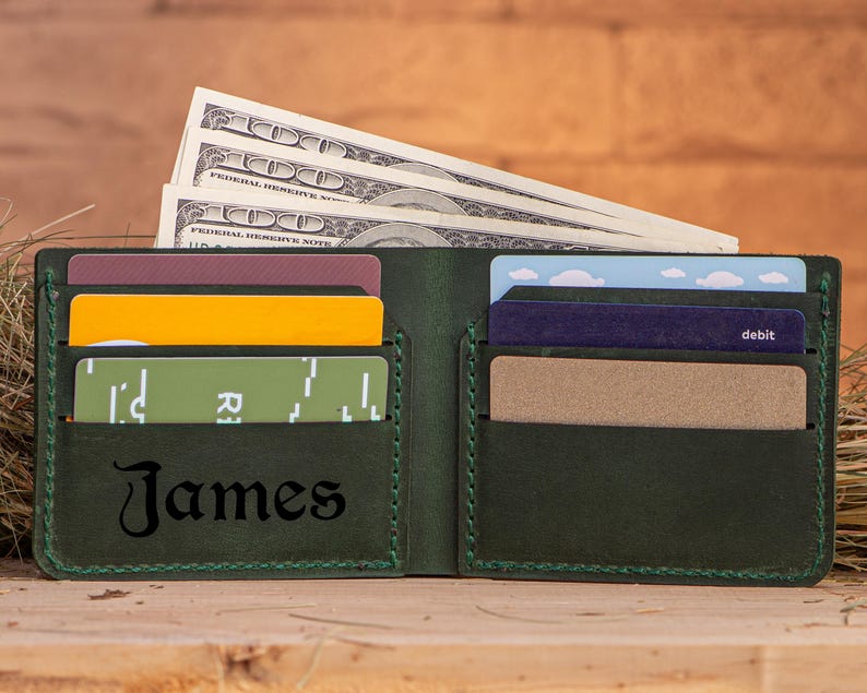 May include: A dark green leather wallet with a stitched border. The wallet has multiple card slots and a cash pocket. The name "James" is embossed on the front of the wallet.
