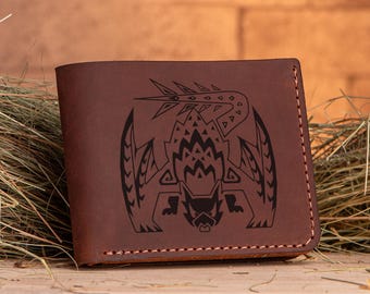 Puede incluir: Una cartera de cuero marrón con un diseño negro grabado detallado de una criatura mítica. La criatura tiene una espalda espinosa, dientes afilados y una expresión feroz.