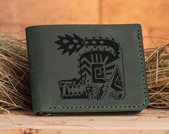 Puede incluir: Una cartera de cuero verde con un gráfico en blanco y negro de una criatura mítica. La cartera tiene un borde cosido.