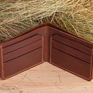 May include: A brown leather wallet with multiple card slots and a billfold. The wallet is open and lying on a wooden surface.