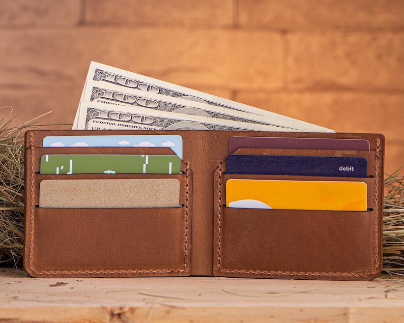 May include: A brown leather wallet with multiple card slots and a cash compartment. The wallet is open and contains cash and credit cards. The wallet is sitting on a wooden surface.