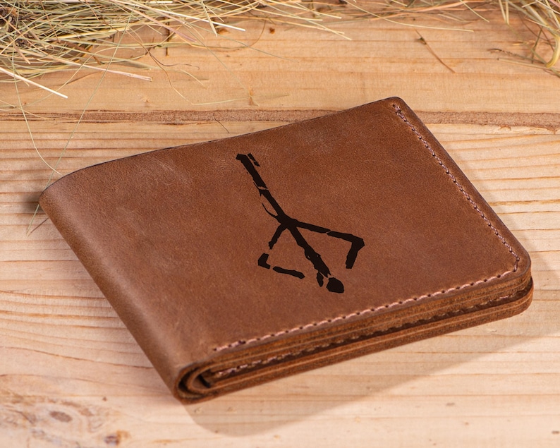 May include: A brown leather wallet with a black symbol engraved on the front. The symbol is a stylized representation of a tree with branches.