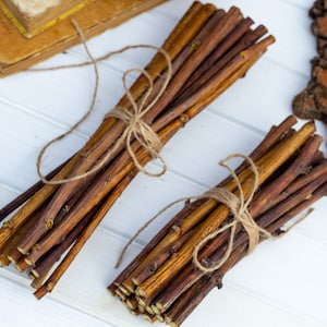 May include: Two bundles of brown twigs tied together with twine. The twigs are approximately 12 inches long and are perfect for crafting or decorating.