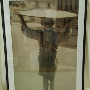 Peut inclure: Une photo en noir et blanc d'un jeune garçon portant un grand plateau rond sur la tête. La photo est encadrée d'un cadre noir et porte le texte "Family Trip to the Village Bakery - January '45" et "Don't Worry, Phil".