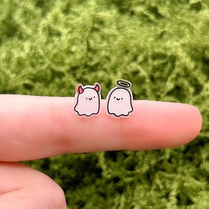 Può includere: Un paio di orecchini a forma di fantasma. Un orecchino presenta un fantasma con corna da diavolo, e l'altro ha un'aureola. Entrambi i fantasmi hanno una faccia sorridente. Gli orecchini sono rosa con contorni neri.