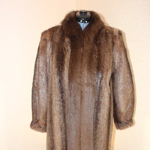 May include: A long brown fur coat with a collar. The coat is on a mannequin and has a straight cut.