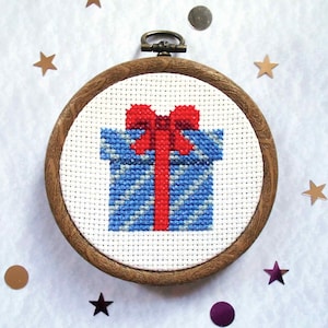 May include: A blue and white patterned gift box with a red bow, framed in a wooden hoop. The gift box is a cross-stitch design.