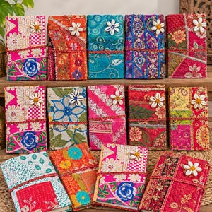 Può includere: Una collezione di quattordici diari rettangolari con copertine in tessuto trapuntato in colori vivaci come rosa, arancione, verde acqua e rosso. Ogni diario è decorato con intricati ricami floreali, motivi patchwork e un fiore di conchiglia bianco.