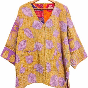 Könnte beinhalten: Eine Jacke mit V-Ausschnitt in Senfgelb mit einem sich wiederholenden Muster aus hellvioletten Blättern. Das Kleidungsstück weist durchgehend sichtbare weiße Kantha-Nähte auf, mit einem kontrastierenden orange-violetten Blumenmuster im Innenfutter.