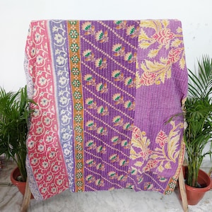 Peut inclure: Un jeté de lit rectangulaire présentant un motif patchwork avec des panneaux verticaux. Le tissu affiche des motifs floraux vibrants dans des tons de rose, violet, orange et vert, accentués par des surpiqûres blanches visibles.