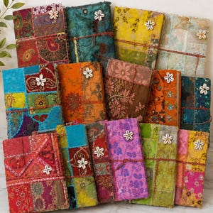 Könnte beinhalten: Eine Sammlung rechteckiger Notizbücher mit Patchwork-Stoffeinbänden in verschiedenen Farben wie Rot, Blaugrün, Gelb, Orange, Pink und Grün. Jedes Notizbuch ist mit einer dünnen Kordel verschlossen und mit einer einzelnen weißen Kaurimuschel verziert.