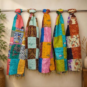 May include: Five rectangular fabric throws hanging on a metal rod. Each throw features a patchwork design with varied colours including pink, yellow, teal, orange, and green, decorated with intricate patterns, floral motifs, and stitched textures.