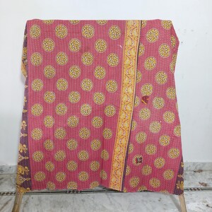 May include: A rectangular quilt featuring a deep pink base with a repeating pattern of yellow circular motifs containing white shapes. The quilt has a vertical yellow border with a paisley design and dark purple edges with yellow floral patterns.