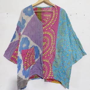 May include: A loose-fitting jacket featuring a patchwork design with various patterns in shades of blue, purple, pink, and yellow. The garment has a V-neckline, wide sleeves, and a single patch pocket on the front, all finished with white running stitch detailing.