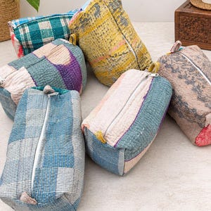 Puede incluir: Un conjunto de seis estuches rectangulares con cremallera hechos de tela acolchada con costuras kantha. Los estuches presentan varios patrones y colores, incluyendo cuadros azules, amarillo, morado y marrón, cada uno con un cierre de cremallera blanco.
