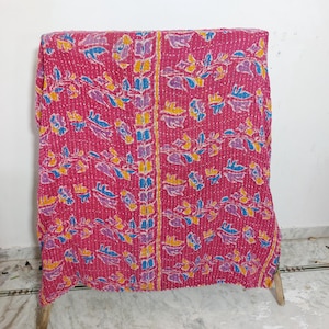Puede incluir: Un textil rectangular con una base de color magenta vibrante y un patrón repetitivo de motivos florales y de hojas estilizadas en amarillo, azul claro y morado. La tela está cubierta en su totalidad por un fino bordado de puntada recta blanca.