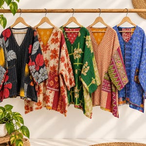 May include: Five long-sleeve tunics with V-necks, each featuring distinct colorful patterns and visible kantha-style stitching. The garments are displayed on wooden hangers, showcasing a variety of floral, geometric, and abstract prints.