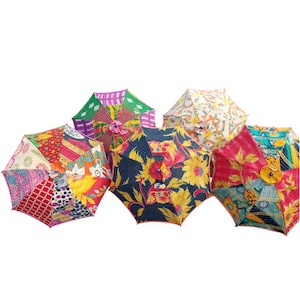 Puede incluir: Un conjunto de paraguas abiertos con coloridos diseños de patchwork. Cada paraguas presenta un patrón único, incluyendo motivos florales, geométricos y abstractos en varios colores como rojo, amarillo, azul y verde. Los paraguas están dispuestos sobre un fondo blanco.