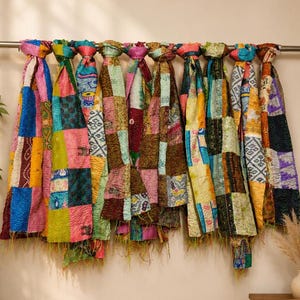 May include: A collection of ten rectangular fabric throws hanging from a horizontal metal rod. Each throw features a patchwork design composed of various colorful textile squares with intricate patterns, visible stitching, and frayed bottom edges.