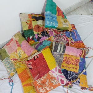 Pode incluir: Uma coleção de almofadas de chão quadradas com um design de patchwork feito de vários tecidos coloridos com costuras kantha visíveis. Cada almofada inclui laços de tecido nos cantos e apresenta uma mistura de padrões florais e geométricos.