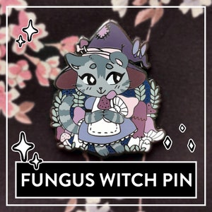 Könnte beinhalten: Eine graue Katze mit einem lila Hexenhut und einem blauen Kleid hält einen Pilz. Die Katze ist von Pilzen und Grün umgeben. Der Text "FUNGUS WITCH PIN" befindet sich am unteren Rand des Bildes.